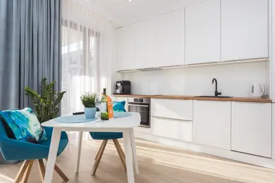 a white kitchen with a white table and blue chairs at City of the Kings - Smile Apartment in Kraków