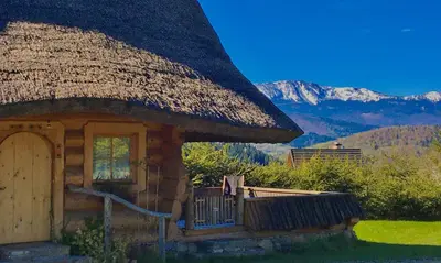 a hut with a thatched roof with mountains in the background at Osada Beskidzka in Zawoja