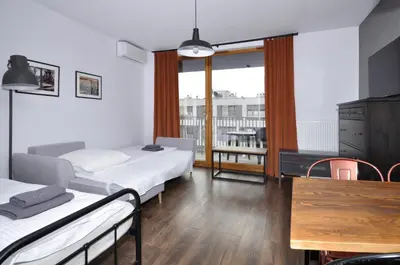 a room with two beds and a table and a balcony at Schindler’s Factory Zabłocie Deluxe Apartments WAWELOFTS in Kraków