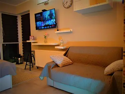 a living room with a couch and a tv on the wall at Cracovia Garden Nowa 5 Dzielnica in Kraków