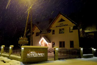 a building in the snow in front of a fence at Willa Modrysówka in Zawoja