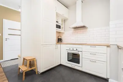 a white kitchen with white cabinets and a stool at City of the Kings - Leaf Apartment in Kraków