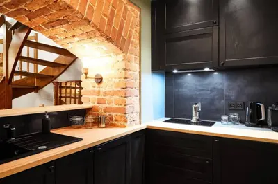 a kitchen with black cabinets and a brick wall at HOUSEHOST Apartment II: Studencka Street in Kraków