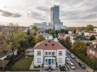 a white house in a city with a tall building at Wesoła by Landmark Apartments in Kraków