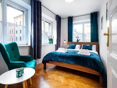 a bedroom with a bed and a chair and windows at CracWoW St. Thomas Apartment in Kraków