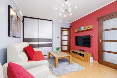 a living room with a white couch and a red accent wall at Apartments Obopólna Cracow by Noclegi Renters in Kraków