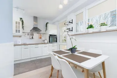 a white kitchen with a wooden table and white chairs at Apartments Obopólna Cracow by Noclegi Renters in Kraków