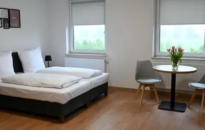 a bedroom with a bed and a table and two windows at ZatorHome apartamenty - blisko Energylandii i Zatorlandu in Zator