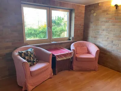 two chairs and a table in a room with two windows at Domek w Lesie in Łęki