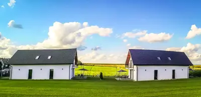 two white houses in a green field with a cloudy sky at Blue Sky - Apartamenty Premium Zator in Zator