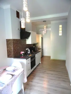 a kitchen with white cabinets and a wooden floor at Apartament Orchidea in Kraków