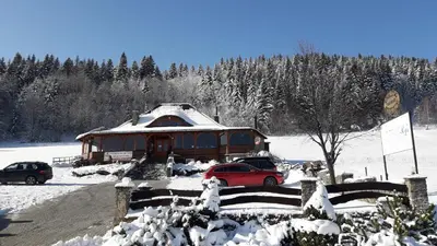 a house with a red car parked in the snow at Domki Karczma Zbójnicka in Wiśniowa