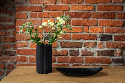 a black vase with flowers on a table next to a brick wall at Szpitalna 9 Residence in Kraków
