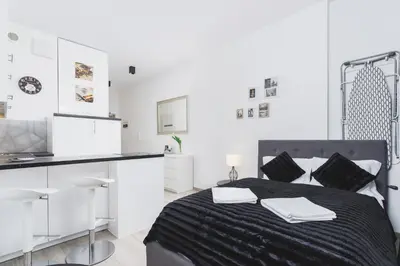 a white bedroom with a black bed and a kitchen at Studios Lubelska Kraków by Noclegi Renters in Kraków