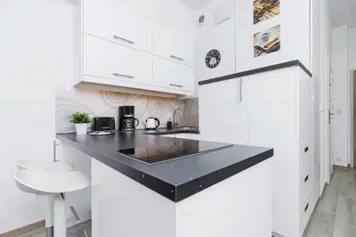 a kitchen with white cabinets and a black counter top at Studios Lubelska Kraków by Noclegi Renters in Kraków