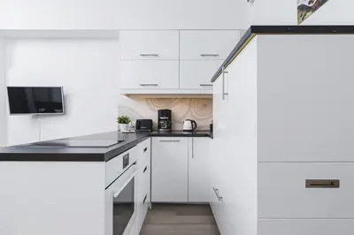 a white kitchen with white cabinets and black counter tops at Studios Lubelska Kraków by Noclegi Renters in Kraków