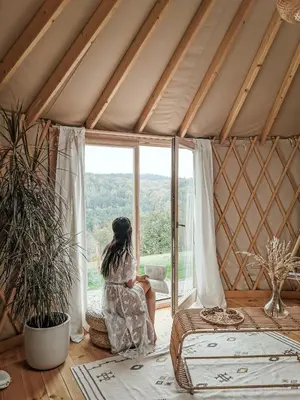 a woman sitting in a room looking out the window at LushHills - Nowoczesna Jurta in Regulice