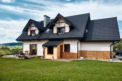 a house with a black roof on a green lawn at Apartament Turbacz in Klikuszowa