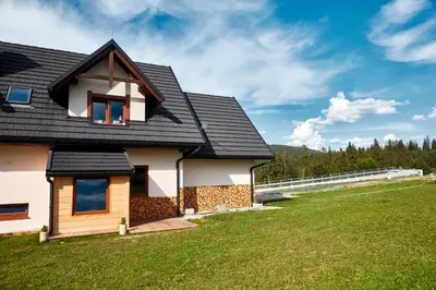 a house with a black roof and a green yard at Apartament Turbacz in Klikuszowa