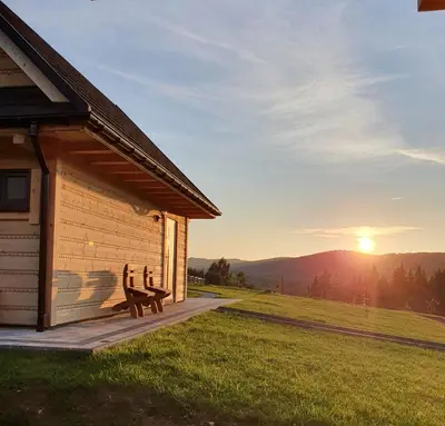 a bench on a deck next to a cabin with the sunset at Ostoja Jaworskie in Stryszawa