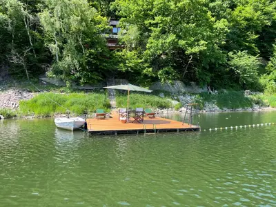 a dock with chairs and an umbrella on the water at Rożnów domek pod Zamkiem in Rożnów