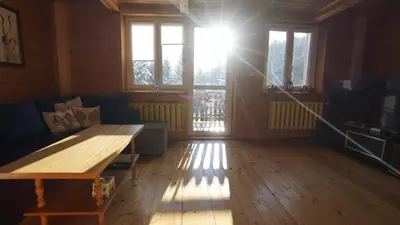 a living room with a wooden table and a sun shining through windows at Zawoja Dom Czatoża in Zawoja