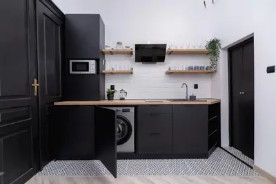 a kitchen with black cabinets and a washer and dryer at Apartment Joselewicza Cracow Kazimierz by Noclegi Renters in Kraków