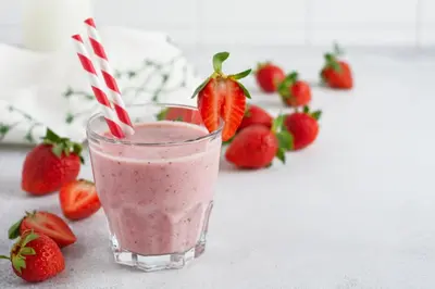 a glass of strawberry smoothie with strawberries in the background at Beautiful studio for couples with Air Conditioning - Old Town & Main station in Kraków