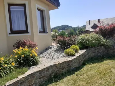 a stone retaining wall next to a house with flowers at Dom w okolicach Czchowa in Wytrzyszczka