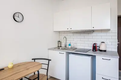 a kitchen with white cabinets and a table and a clock at Mickiewicza Old Town Apartment WAWELOFTS in Kraków