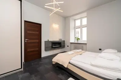 a white bedroom with a large bed and a fireplace at Apartament Papieski in Wadowice