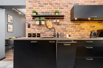 a kitchen with black cabinets and a brick wall at Old Town Studio Good Vibes by Noclegi Renters in Kraków