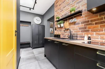 a kitchen with black cabinets and a brick wall at Old Town Studio Good Vibes by Noclegi Renters in Kraków