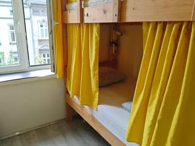 a bunk bed with yellow curtains in a room with a window at Evergreen Hostel Krakow in Kraków