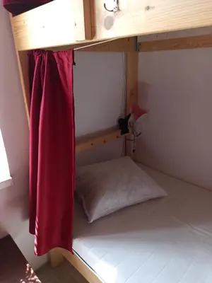 a bunk bed with a red curtain and a pillow at Evergreen Hostel Krakow in Kraków