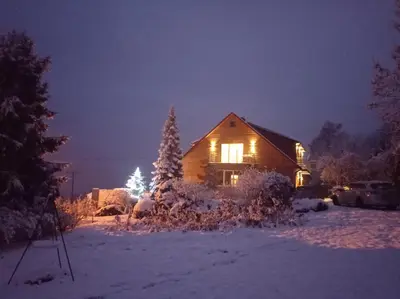 a house with a christmas tree in the snow at night at Noclegi Leśniczówka w Lanckoronie in Lanckorona