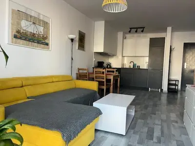 a living room with a yellow couch and a kitchen at APARTAMENT HELSINKI in Kraków