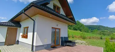 a small white house with two chairs and a table at Domki pod Groniem in Kasina Wielka