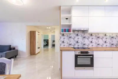 a kitchen with white cabinets and a living room at ZATOR Apartamenty Max House, Energylandia in Zator
