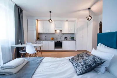 a bedroom with a bed and a kitchen with white cabinets at Drwinka Park Apartment in Kraków