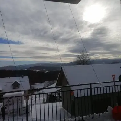 a snow covered hill with a building and a fence at Michalka 2 - Domki pod Leskowcem in Targoszów