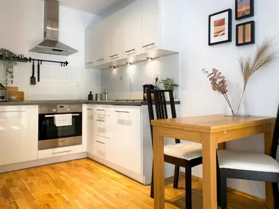 a kitchen with white cabinets and a wooden table with chairs at Charming Studio for couples in the heart of Cracow in Kraków