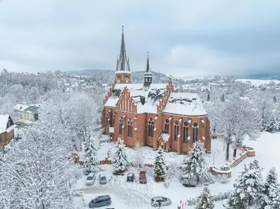 a church covered in snow with cars parked in front at Slow Life Rabka in Rabka