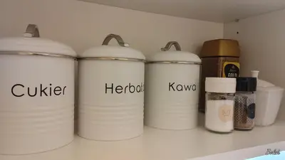 a row of white containers on a shelf with spices at Mieszkanko na peryferiach in Chrzanów