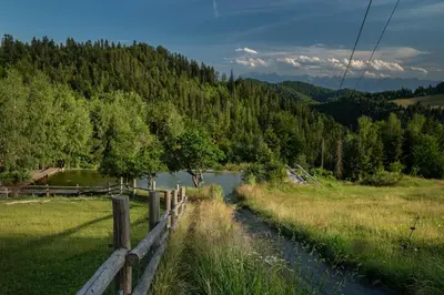 a fence next to a river in a field at Górna Chata Mountains Chalet - Stable Cottage in Ochotnica Górna