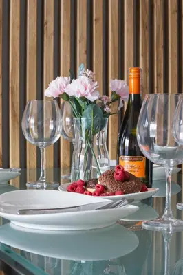 a table with a plate with a vase of flowers and wine glasses at Lotniczówka Apartments by Renters Prestige in Kraków