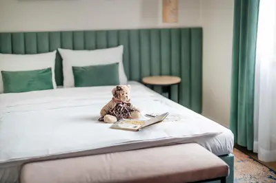 a teddy bear sitting on a bed with a book at Hotel H12**** in Kraków