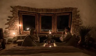 a man and woman sitting in chairs in a room with a candle at Domek Hobbita z jaskinią SPA - Osada Jaworzyny in Tokarnia