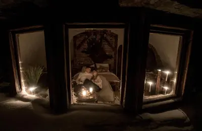 a bride and groom sitting in the snow with candles at Domek Hobbita z jaskinią SPA - Osada Jaworzyny in Tokarnia