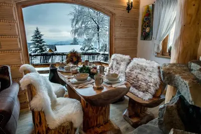 a living room with a table and a large window at Baśniowy Domek Groń z Jaskinią SPA - Osada Jaworzyny in Tokarnia